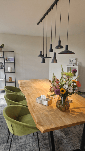 Gespreksruimte met grote houten tafel, zes lichtgroene stoelen en zachte verlichting